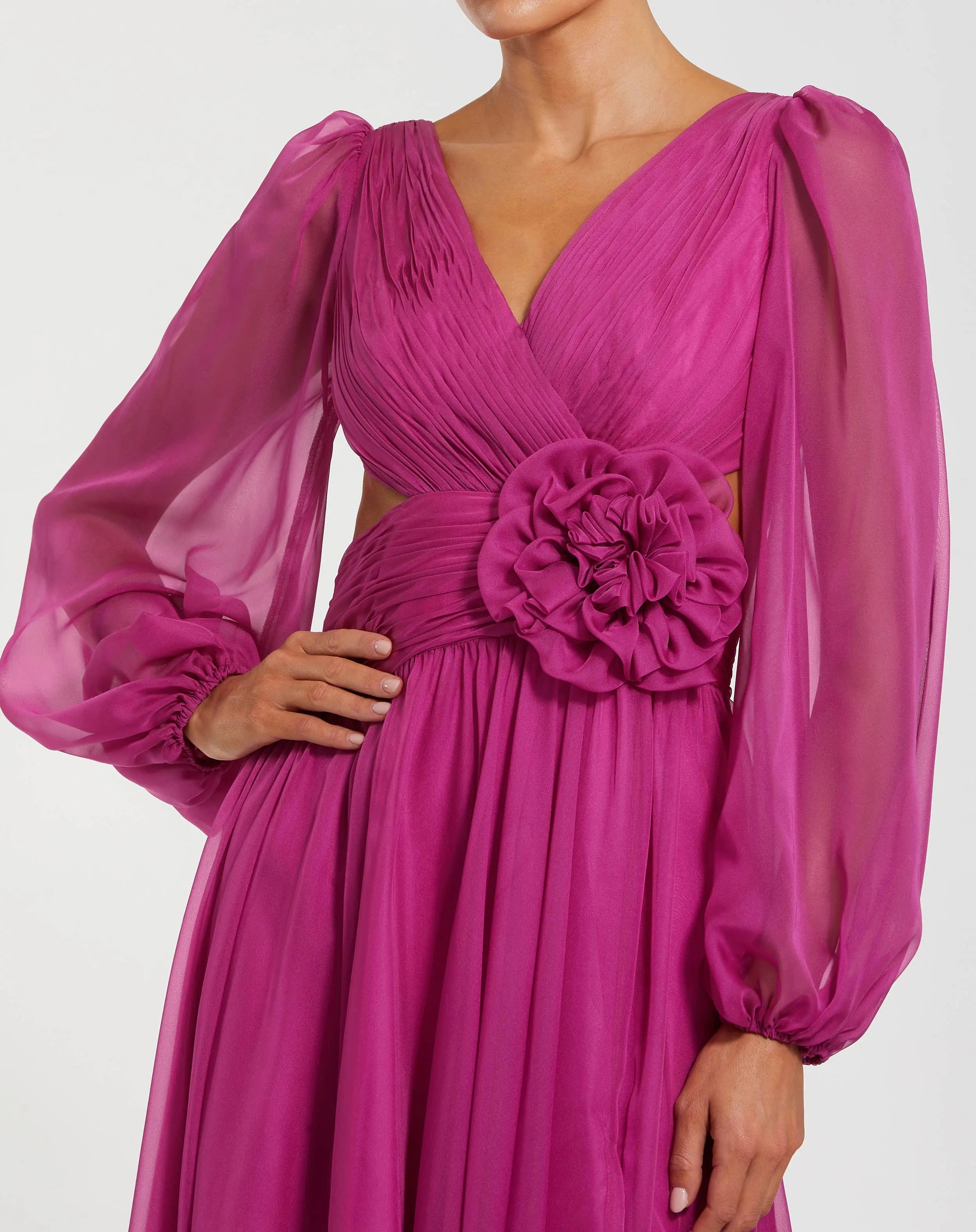 Wearing the Mac Duggal 56072 Long Formal Dress in magenta chiffon, which features sheer long bishop sleeves, a pleated bodice, a cut-out waist, and a statement fabric flower at the center.